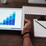 Person Holding White Ipad on Brown Wooden Table